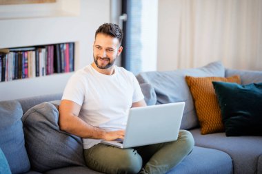Evde dinlenirken laptop kullanan yakışıklı adam..