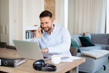 Başarılı bir iş adamı evde çalışırken cep telefonu ve laptop kullanıyor. Merkez Ofis.