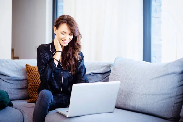 快乐的女人在家里放松的时候用她的笔记本电脑 — 图库照片