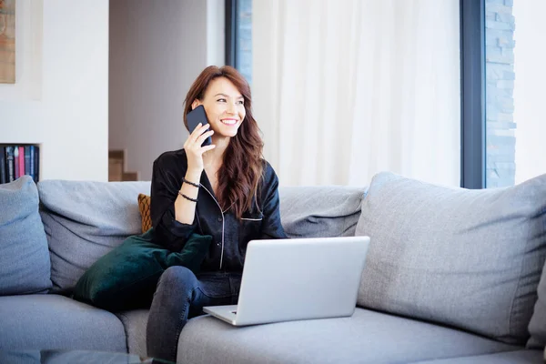 快乐迷人的女人在家里工作时使用手机和笔记本电脑 总部办公室 — 图库照片