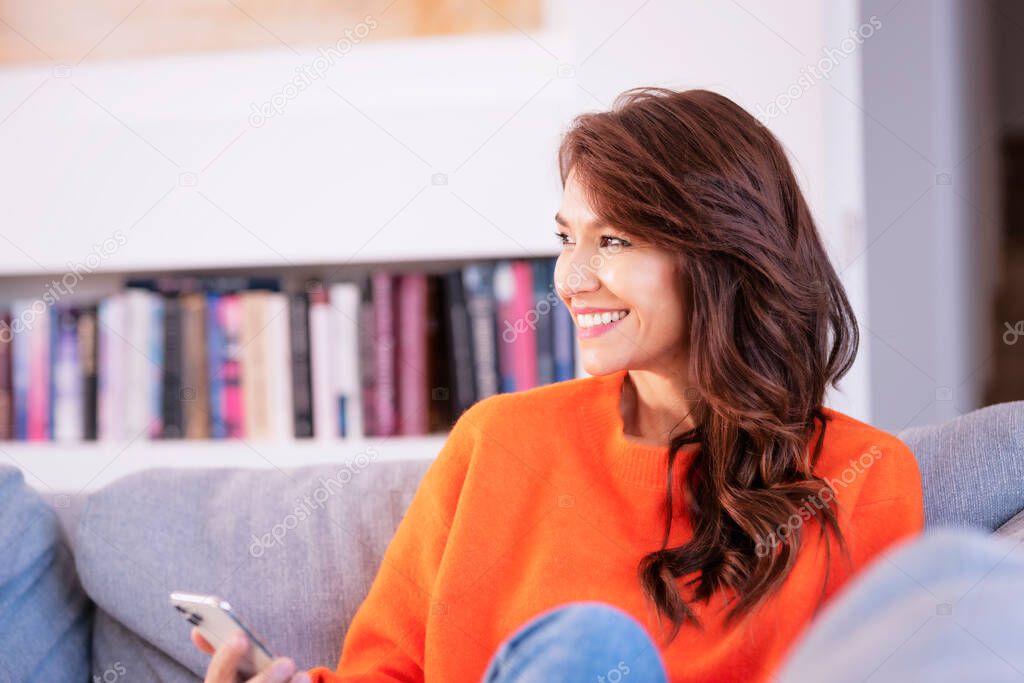 Shot of an attractive and happy woman using her smartphone and text messaging while relaxing on the couch at home. 