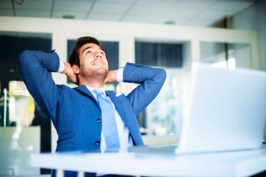 Relaxed businessman wearing suit while sitting at desk in the office leaning back. 