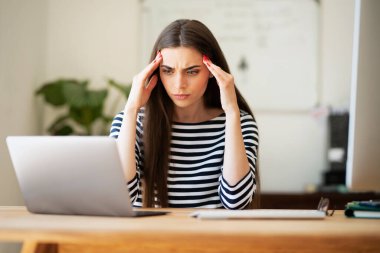 Female entrepreneur with headache sitting at desk. Businesswoman under terrible physical tension at work. Home office.