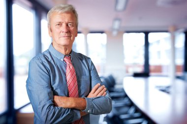 Executive senior businessman standing with arms crossed in a boardroom. 