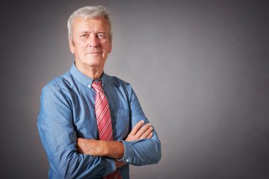 Studio portrait of senior businessman wearing shirt and tie while standing at isolated grey background. 