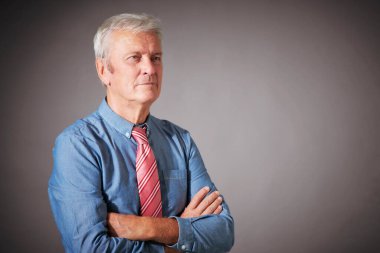 Studio portrait of senior businessman wearing shirt and tie while standing at isolated grey background. 