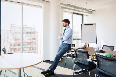 Full length shot of thinking businessman standing at the office. Professional man wearing shirt and tie while standing with arms crossed.