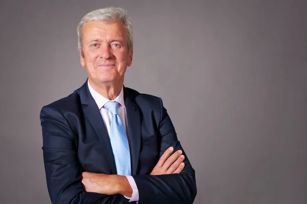 Closle-up studio portrait of grey haired businessman wearing suit while standing at isolated grey background. Copy space.