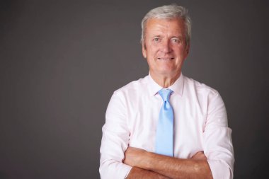 Studio portrait of senior businessman wearing shirt and tie while standing at isolated grey background. 