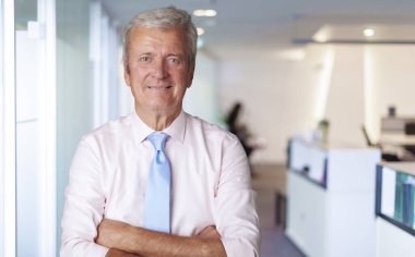 Executive senior businessman standing with arms crossed in a boardroom. 