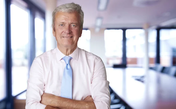 Executive senior businessman standing with arms crossed in a boardroom.