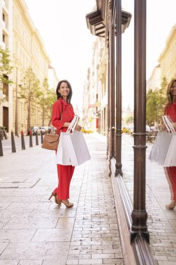 Happy middle aged woman with shopping bags walking down the street in the city. City life. 