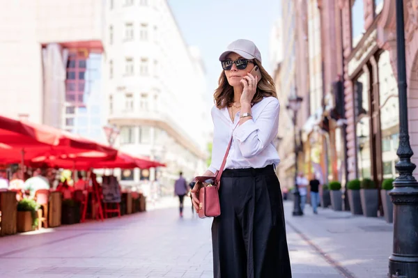 Attractive woman wearing smart clothes and sunglasses while walking in a city and speaking on her mobile phone.