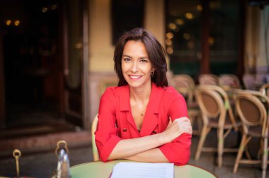 Portrait of an attractive brown haired woman looking at camera and smiling while sitting at outdoor coffee. table