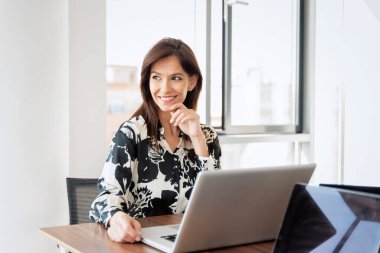 Thinking businesswoman using a laptop at her desk in a modern office while working.