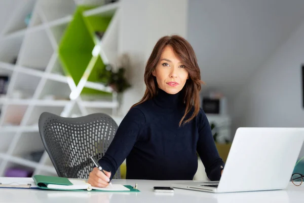 彼女のラップトップの後ろにオフィスデスクに座って 新しいプロジェクトに取り組んでいる間 タートルネックセーターを着て自信を持って中年のビジネスマンの女性 — ストック写真