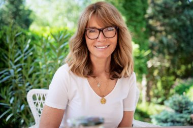 Close-up portrait shot of cheerful middle aged woman wearing glasses and white t-shirt while relaxing on the patio at home.