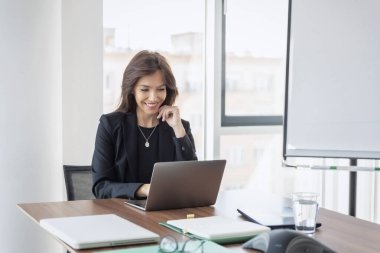 Smiling professional businesswoman talking in front of the camera while having video conference with her business partners on laptop.