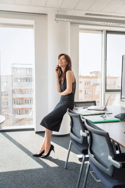 オフィスに座って電話で話す魅力的なビジネスマンの完全な長さ 黒のドレスを着たエグゼクティブ女性 — ストック写真