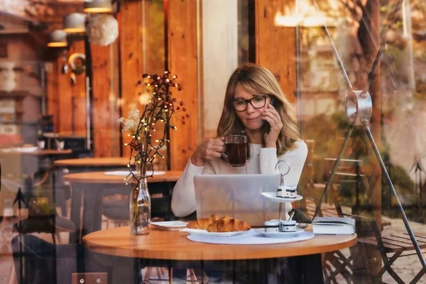 中年妇女笔记本电脑和智能手机在咖啡店 在网上工作的女商人 — 图库照片