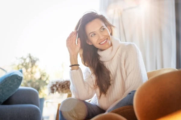 自宅のアームチェアに座っている陽気な女性のショット 自宅でリラックスしながら 魅力的な女性は笑いとセーターを着て — ストック写真