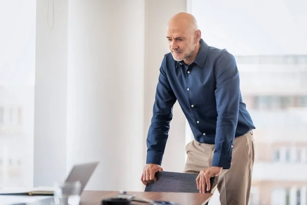 Shot of thinking businessman standing at desk in the office. Professional male wearing shirt.