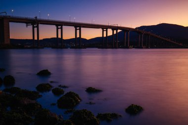 Günbatımında ikonik Tasman Köprüsü açık bir bahar akşamı Hobart, Tazmanya, Avustralya 'daki Derwent Nehri' ni geçer. Clarence 'ın kıyılarından çekildi.