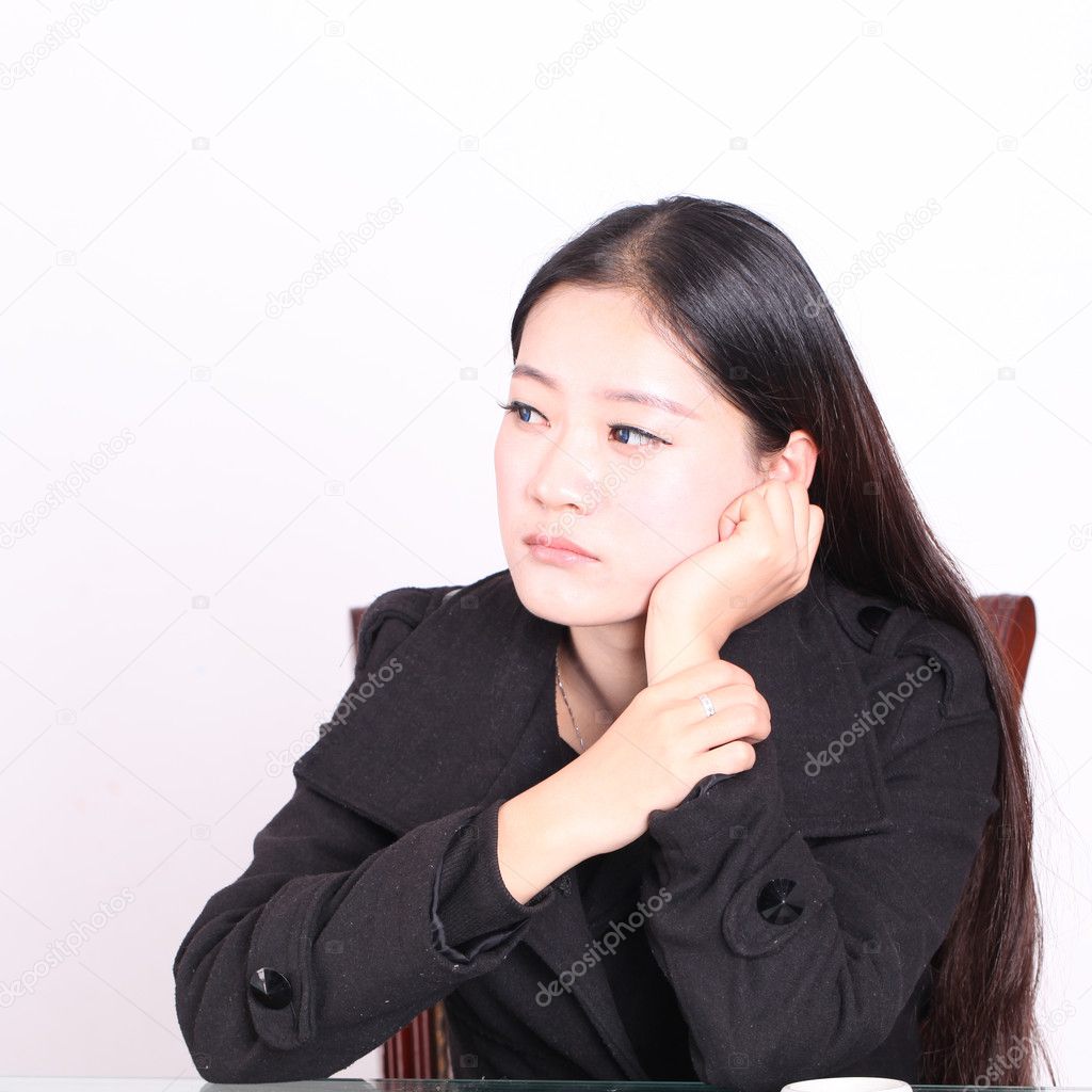 An oriental woman wearing black casual sitting at desk pondering