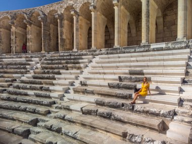 Aspendos amfitiyatrosunda oturan sarı elbiseli hoş bir kadın turist. 