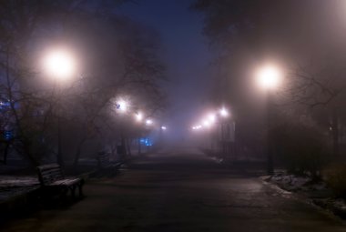 Foggy night park with man's silhouette in the distance. clipart