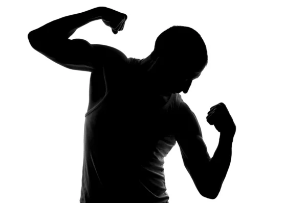 Silhouette of young strong man looking on his biceps. — Stock Photo, Image