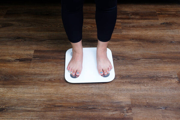Close-up female feet stepping on body weight scale. Weight control, weight loss concept.