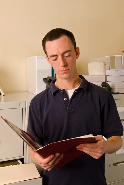 Caucasian male in file room reading papers inside a folder — Stock Photo, Image