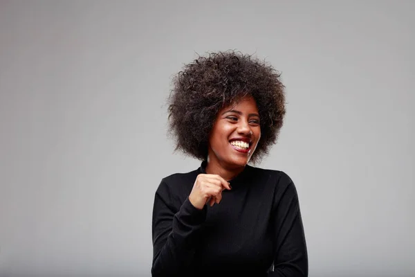 Candid portrait of a giggling young Black woman looking off to the side with an amused expression over a grey background with copyspace