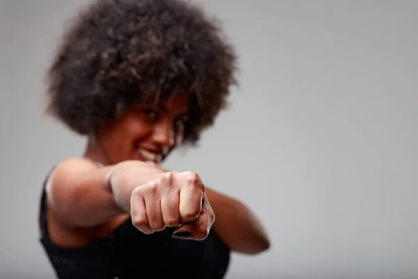Playful young Black woman throwing a punch at the camera with focus to her fist over a grey studio background with copyspace