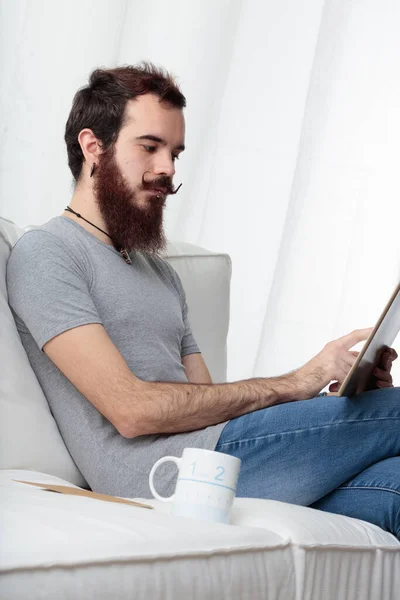 턱수염을 남자는 일하거나 즐기기 인터넷이나 사용하거나 소파에 원격으로 일하는 했습니다 — 스톡 사진