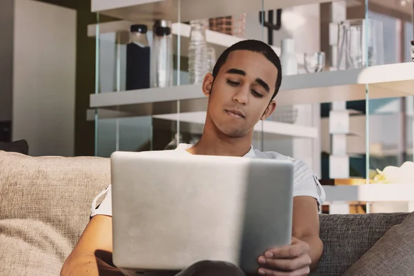 自宅のソファの上で顔と真剣な表情でリラックスしながら 若い男はメディアを見たり ノートパソコンで読んだり — ストック写真