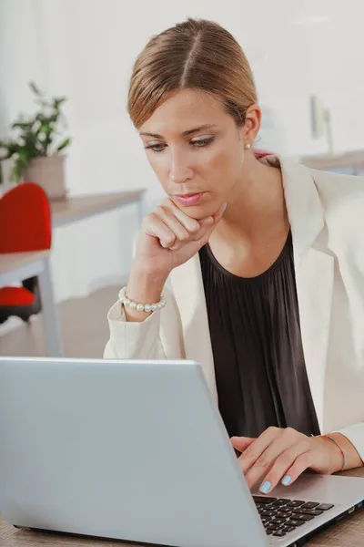 聪明的女商人坐在一个重要的办公室里的办公桌前 双手托着下巴 专心致志地阅读笔记本电脑上的数据 — 图库照片