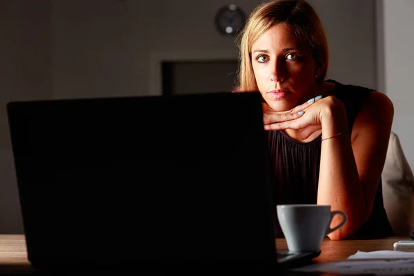 专心致志的女商人工作到深夜 坐在笔记本电脑旁 在黑暗中被屏幕照亮 看着摄像机 — 图库照片