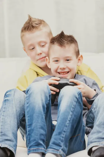 二いたずらな若いです男の子遊びビデオゲーム一緒に上のソファにホームでザ小さな男の子に焦点を当てて前に保持ザジョイスティック — ストック写真