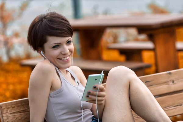 Glückliche Junge Frau Lächelt Genüsslich Während Sie Mit Ihrem Smartphone — Stockfoto