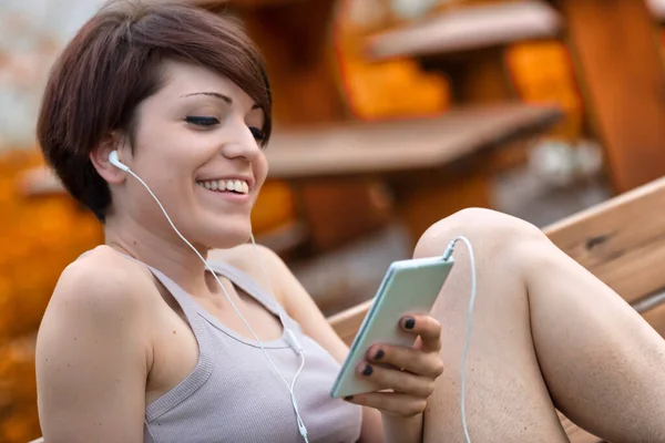 一位快乐的年轻女子一边听着音乐 一边在公园的长椅上近距离地放松自己 一边微笑着 — 图库照片