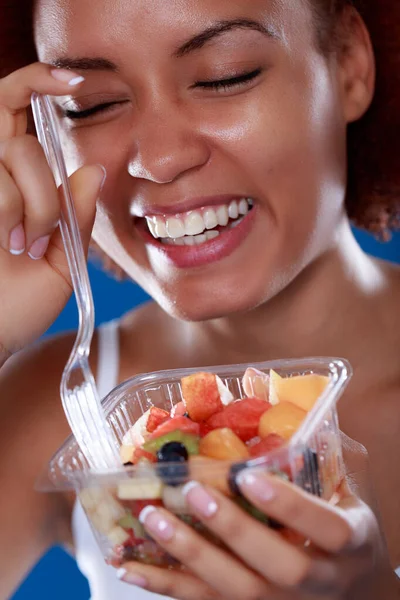 Candid portrait of a laughing vivacious young Black woman eating a fresh fruit salad in a healthy diet concept