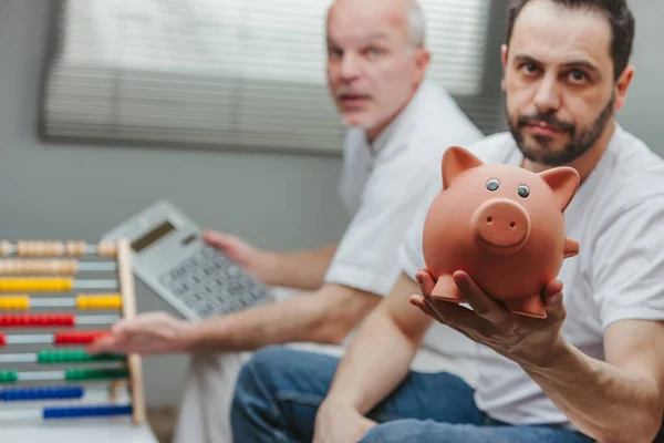Disappointed Man Showing Piggy Bank While His Senior Father Calculating — Stock Photo, Image