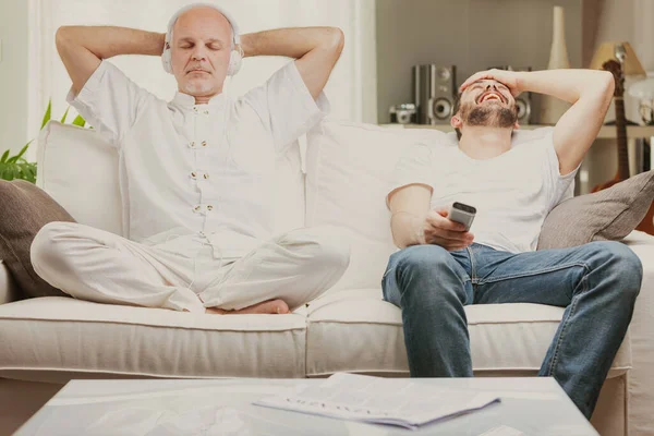 家でリラックスしている2人の男性 音楽を聴きながら静かに瞑想している1人の高齢者 そしてテレビ番組で以前に笑っている1人の若い人 — ストック写真