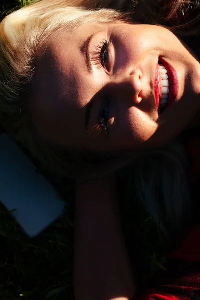 太陽の光の最後の光線の中でカメラを見上げ笑顔ブロンドの女性の影の高いコントラストの肖像画下のコピースペース — ストック写真
