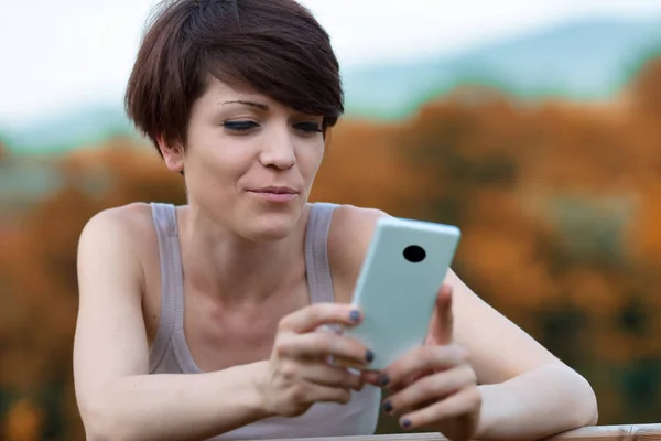 Ung Kvinna Läser Ett Sms Sin Mobiltelefon Med Ett Grinigt — Stockfoto