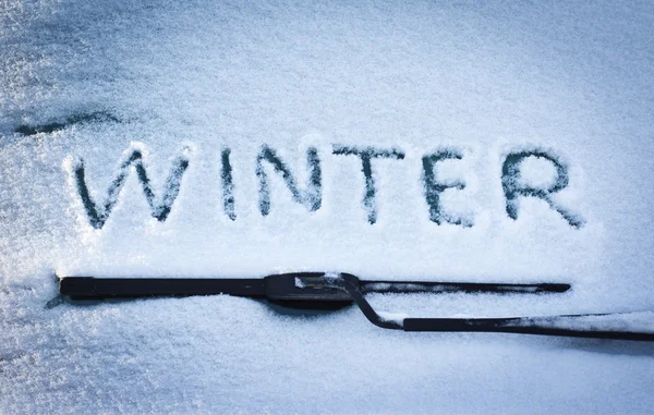 Invierno escrito en nieve en el parabrisas del coche debajo del limpiaparabrisas —  Fotos de Stock