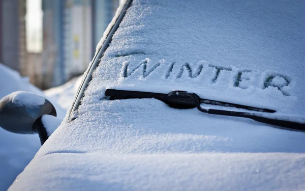 Winter written in snow on car windscreen below windscreen wiper