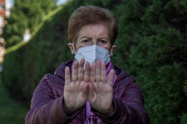 Tıbbi maske takan ve elleriyle dur işareti yapan yaşlı kadın, Coronavirus inkar kavramı.
